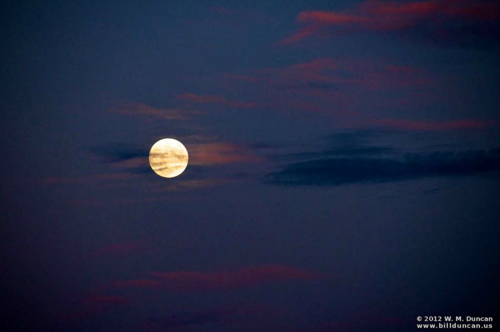 Full moon setting in clouds touched by dawn's early light.