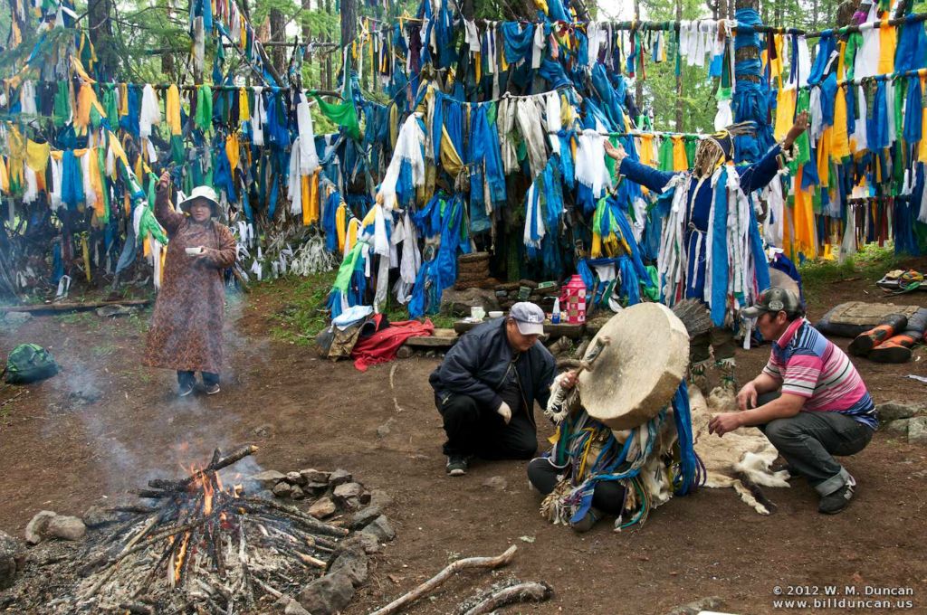 The shaman beats the drum held to her head.  Attendants will protect her if she starts lurching.